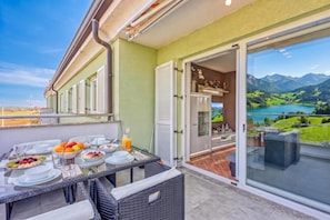 A balcony with a dining table set for breakfast, a view of a lake, and mountains in the distance. - Sea Breeze Residence Mariella (Umag)