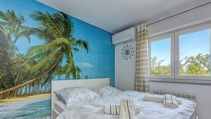 A bedroom with a beach mural, a bed with towels, a window with curtains, and a wall clock. - Sea Breeze Residence Mariella (Umag)