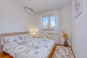 Une chambre à coucher avec un lit, une lampe de chevet, une fenêtre avec des rideaux, un radiateur et un vase avec des fleurs.