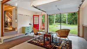 Ein geräumiges Zimmer mit einem großen Schiebeglasfenster, das zu einem überdachten Außenbereich führt, einer Holztreppe und einer grünen Kommode.