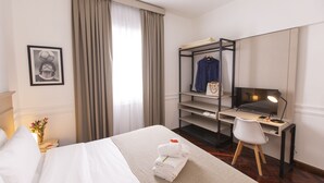 Habitación de hotel con cama, escritorio con silla, armario y un amplio ventanal con cortinas.
