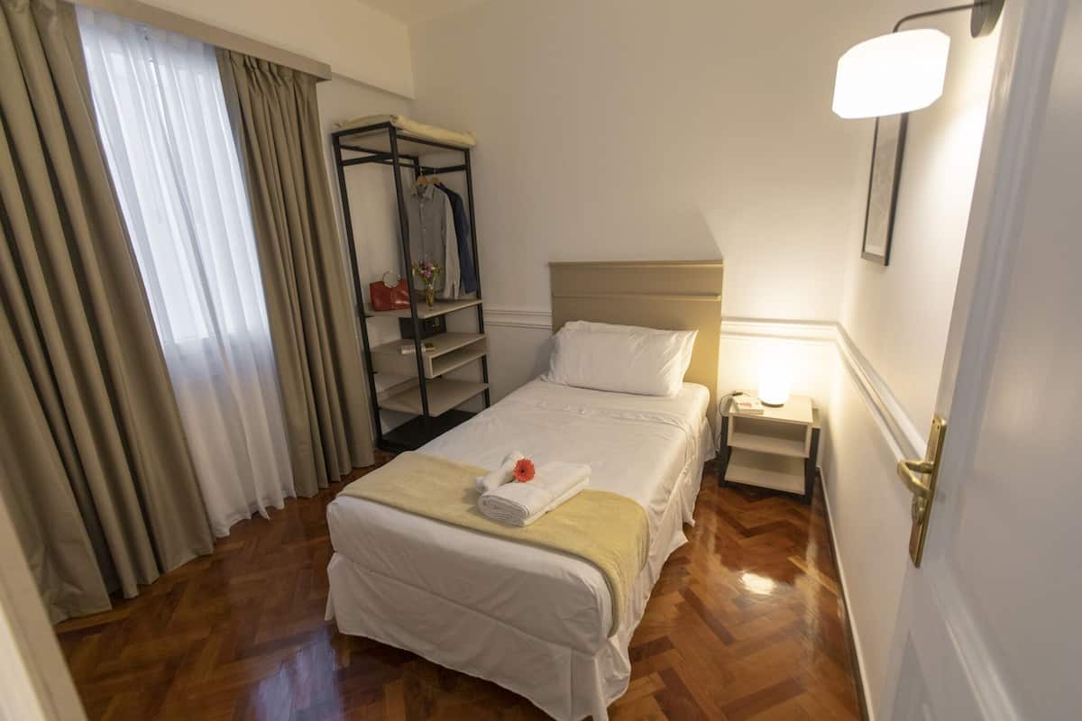 A hotel room with a bed, a nightstand, a wardrobe, and a window with curtains.