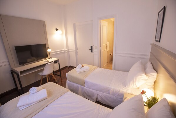 Habitación de hotel con dos camas, un escritorio, una silla y una televisión.