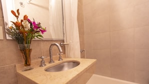 Un baño con lavamanos de mármol, un espejo y una ducha.