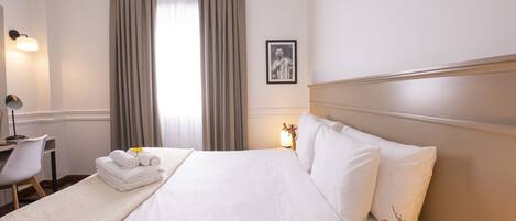 Habitación de hotel con una cama bien hecha, un escritorio con una silla, una lámpara y un cuadro en la pared.