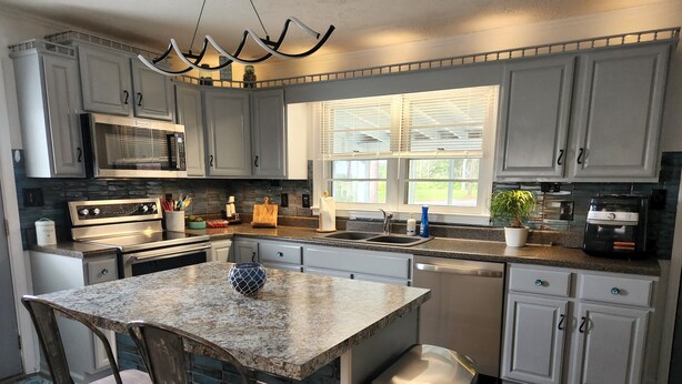 A modern kitchen with granite countertops, stainless steel appliances, and a central island with bar stools. - 2 miles to the beach!!  Full renovated home with ICW views (Supply)