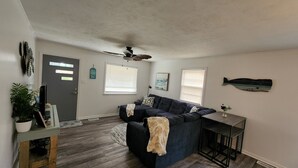 A living room with a dark blue sofa, a ceiling fan, and a fish wall decoration. - 2 miles to the beach!!  Full renovated home with ICW views (Supply)