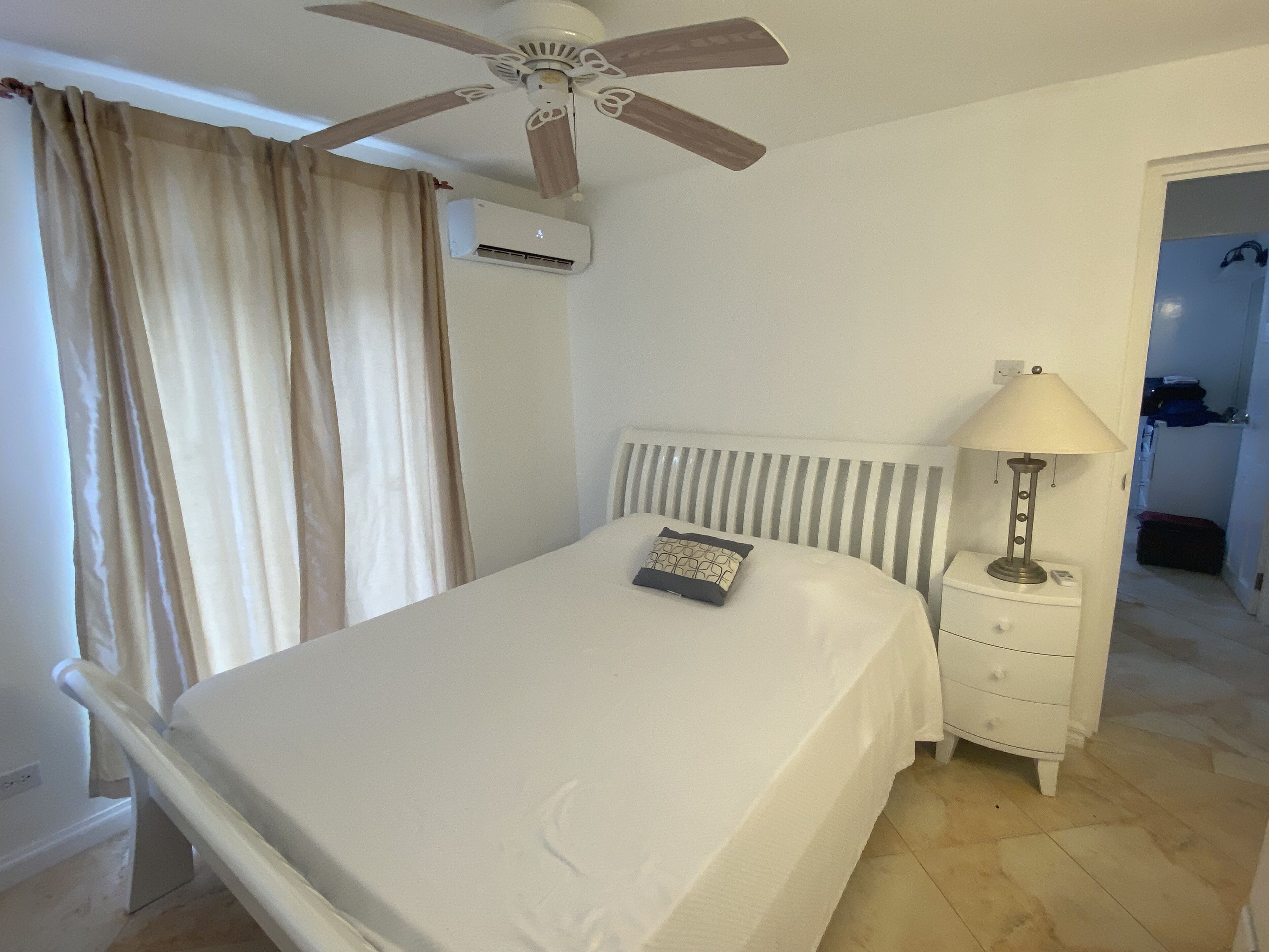 A bedroom with a bed, a nightstand, a lamp, a ceiling fan, and an air conditioning unit.