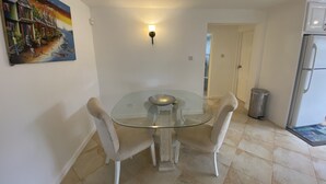 Un coin repas avec une table en verre et des chaises blanches, un tableau au mur et un réfrigérateur à l’arrière-plan.