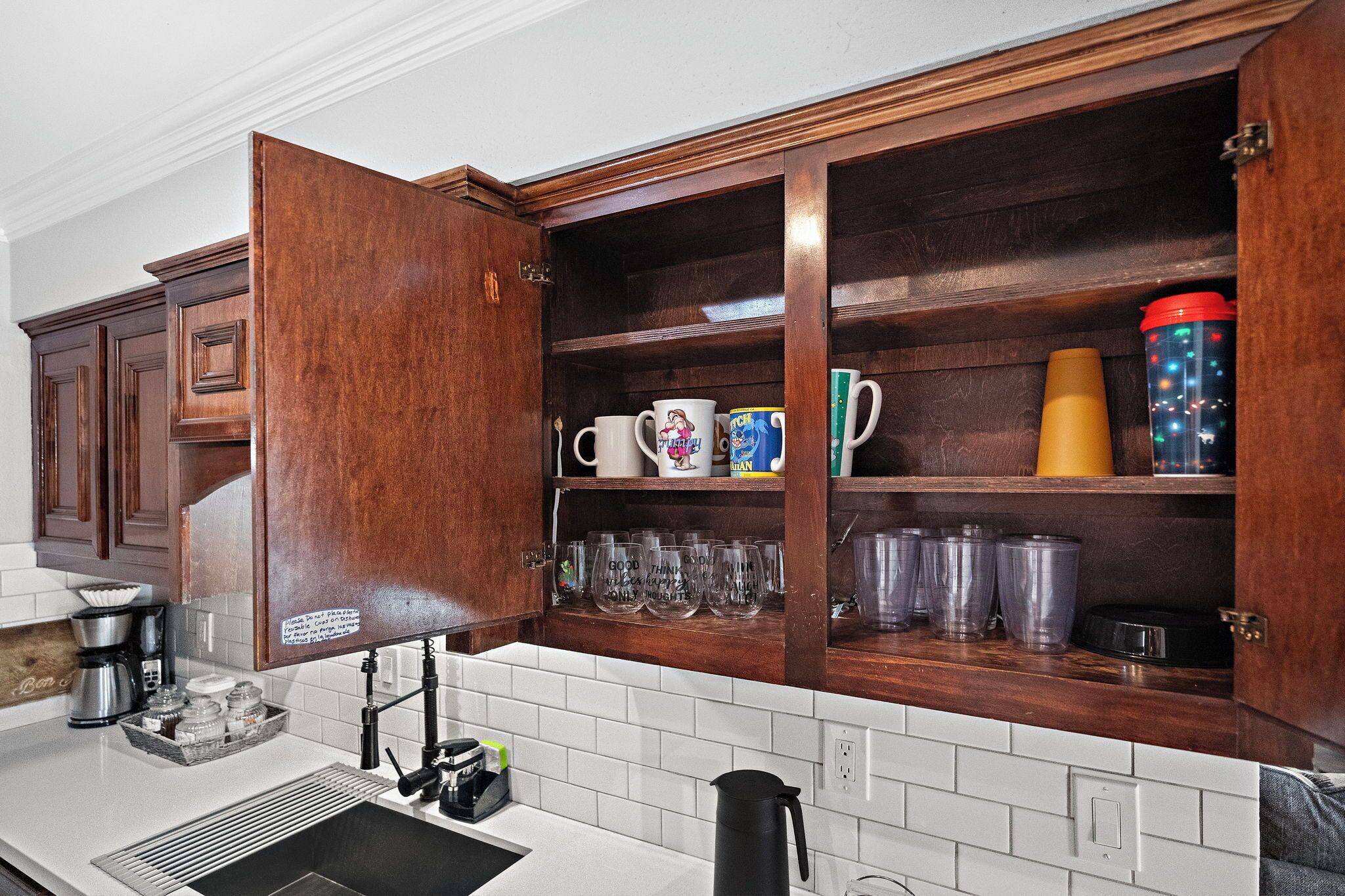 A kitchen with wooden cabinets, a coffee maker, and various mugs and glasses.