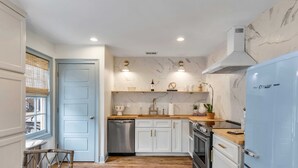Une cuisine moderne avec des meubles blancs, un lave-vaisselle en acier inoxydable, un réfrigérateur bleu et un plan de travail en bois.