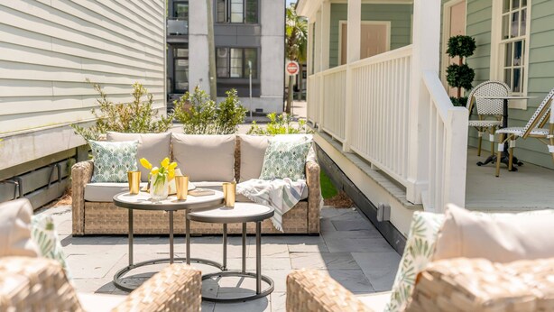 Un espace patio aménagé avec des meubles en osier, une petite table ronde et un canapé confortable agrémenté de coussins à motifs.