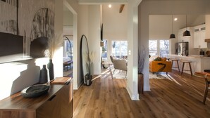 Een moderne keuken met houten vloeren, een zithoek met een gele bank en een groot raam dat voor natuurlijk licht zorgt.