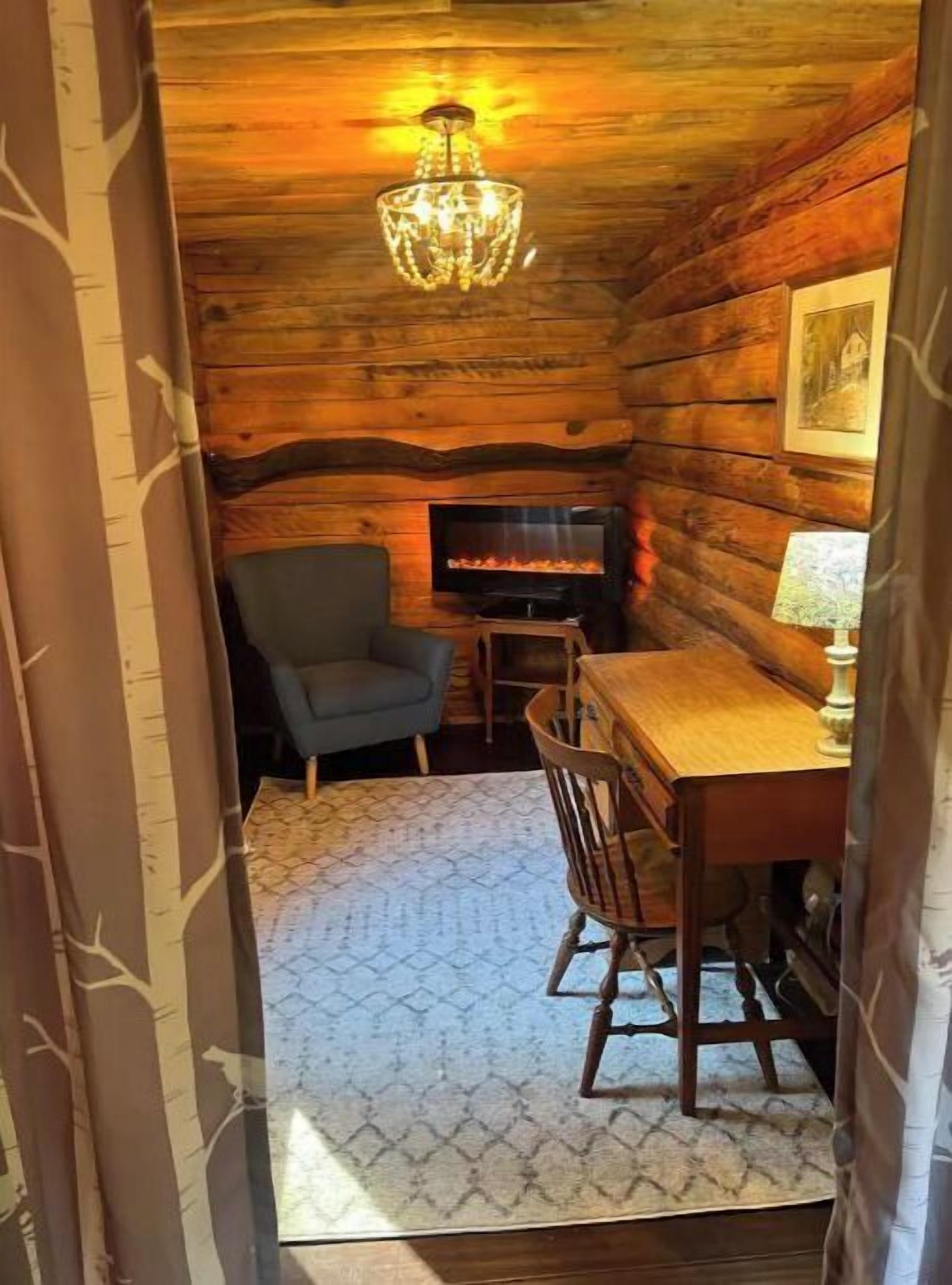 L’intérieur d’un chalet accueillant, avec un mur en bois, un lustre, une cheminée, un téléviseur et une table à manger entourée de chaises.