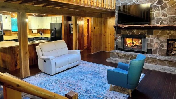 Een gezellige woonkamer met een stenen open haard, een witte bank en een blauwe fauteuil.