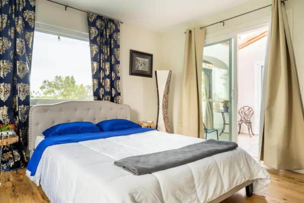 A bedroom with a large bed, a bedside table, a chair, and a view of the outdoors.