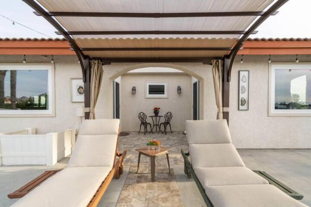 A covered outdoor seating area with two lounge chairs, a small table, and a view of the interior through an archway.