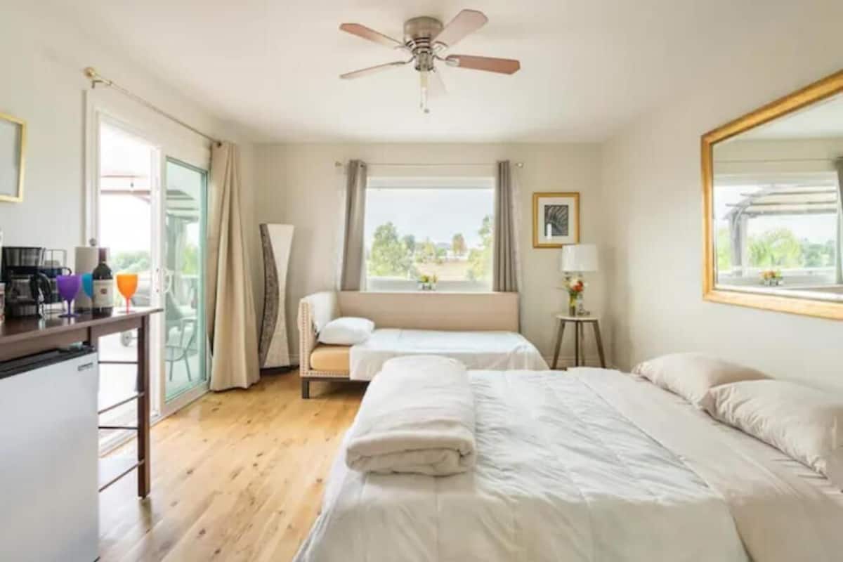 Une chambre d’hôtel équipée d’un lit, d’un bureau, d’une chaise, d’un ventilateur de plafond et d’une fenêtre avec des rideaux.