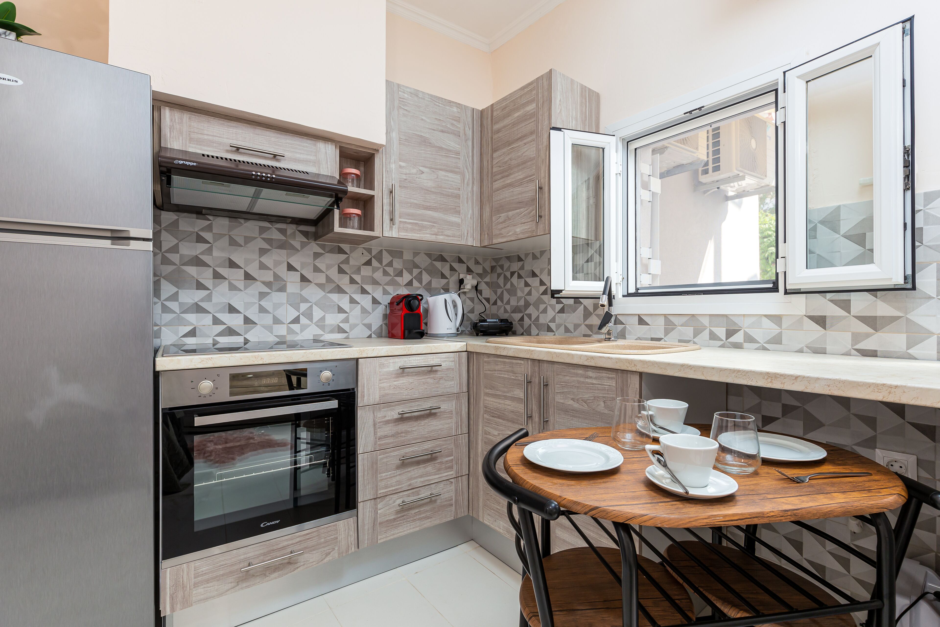 A compact kitchen with a built-in oven, a coffee maker, and a dining table set for two.