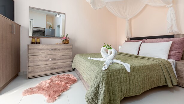 Ein Schlafzimmer mit einem Bett, einer Kommode, einem Spiegel und einem pinkfarbenen, flauschigen Teppich.