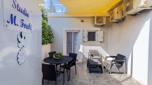 Ein Außenbereich mit Terrasse, Tisch, Stühlen, einem gelben Sonnensegel und Klimaanlagen.