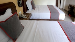 A hotel room with two beds, each with white bedding and red trim. There is a telephone on the nightstand.