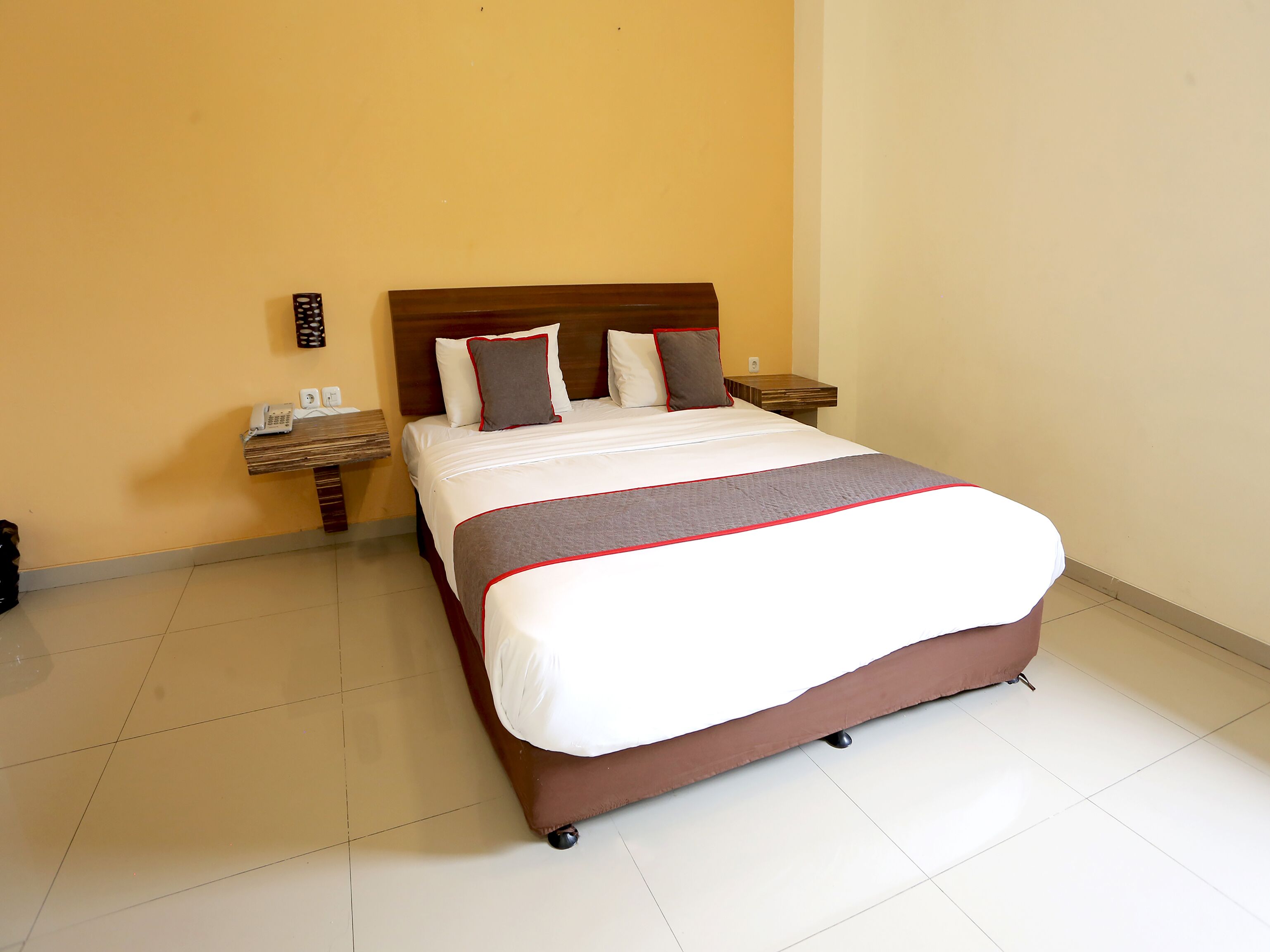 A hotel room with a bed, a nightstand, a phone, and a wall-mounted light.