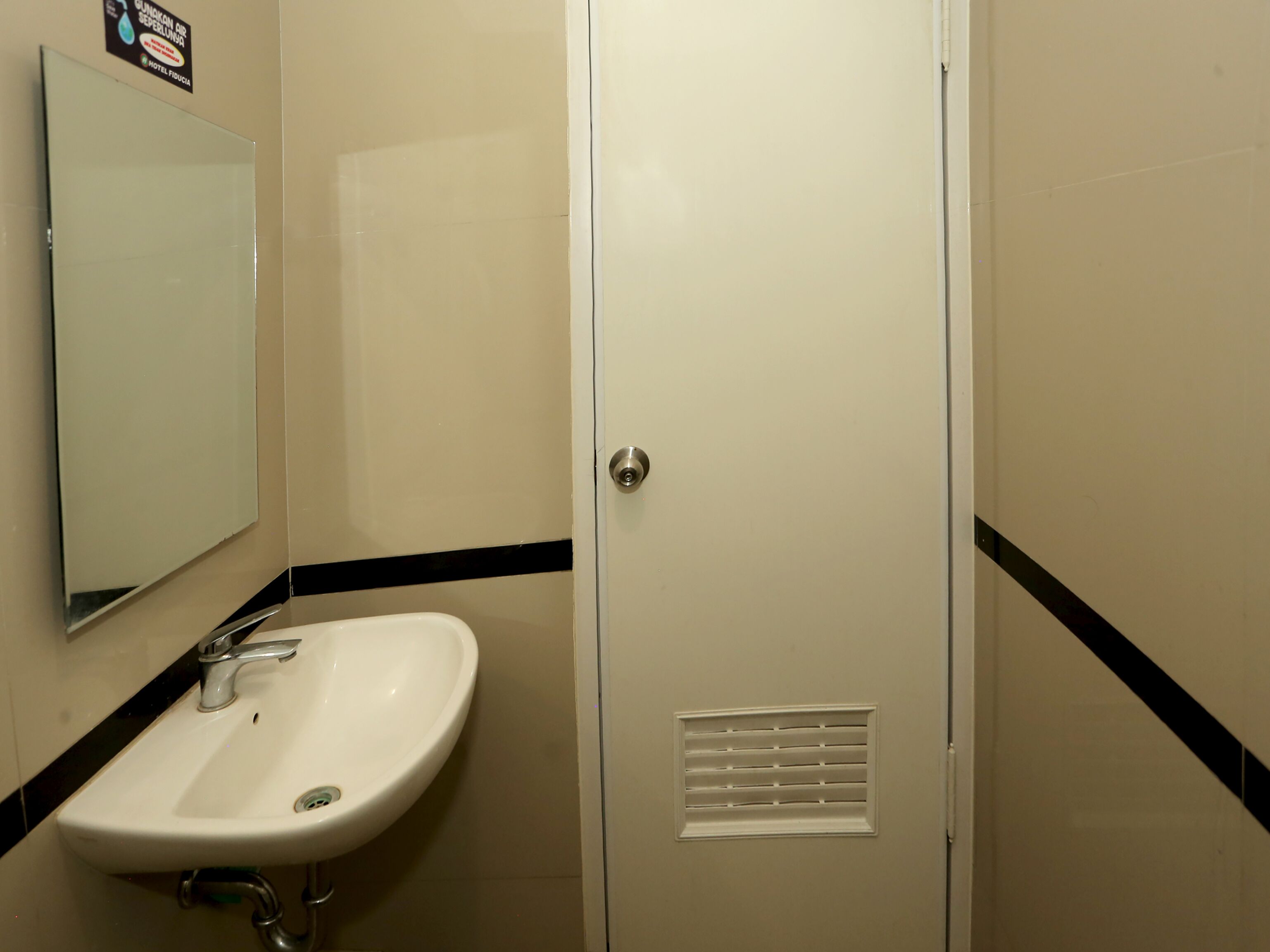 A bathroom with a white sink, a mirror, and a door with a vent.