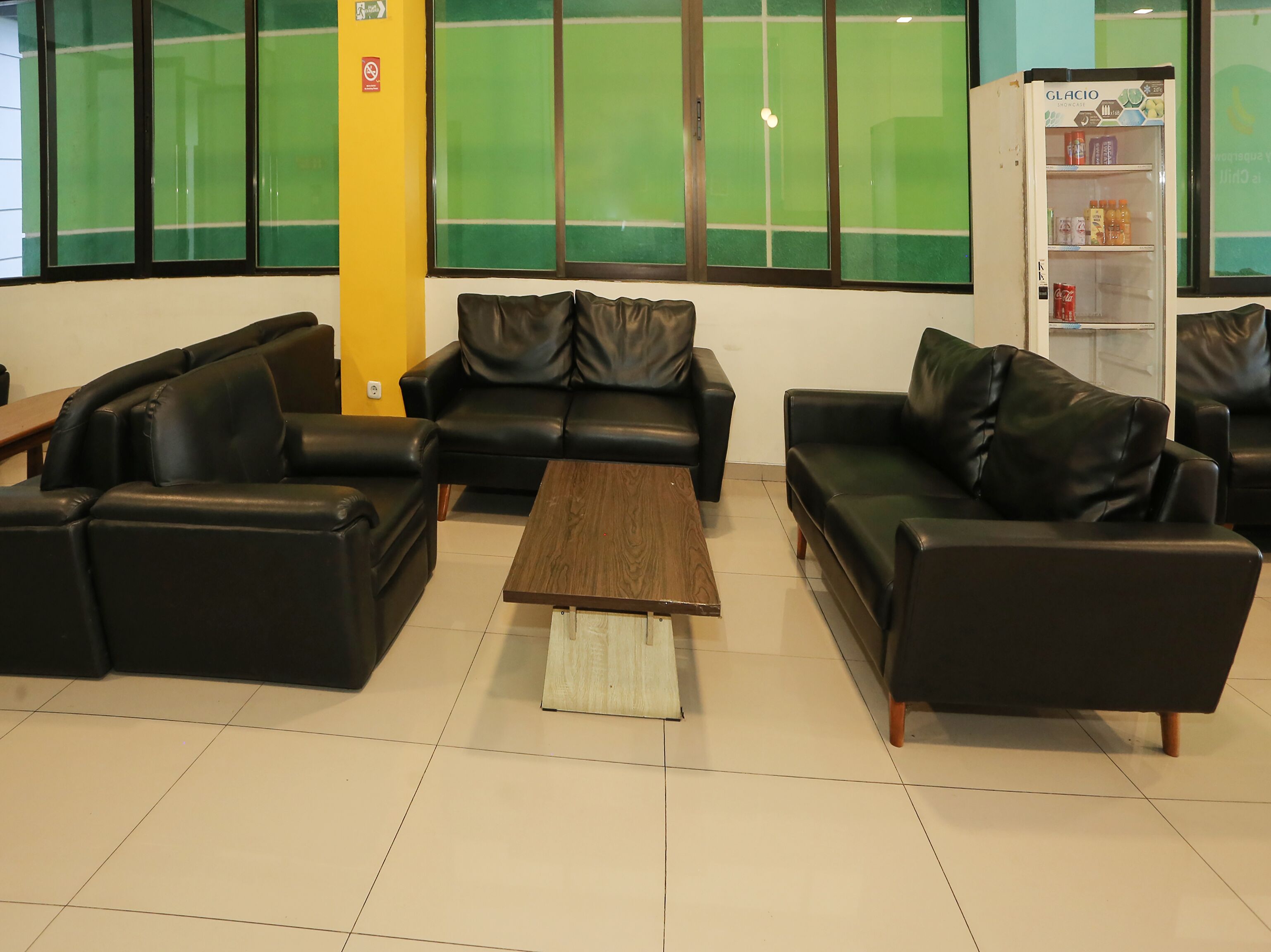 A modern living area with leather sofas, a wooden coffee table, and a refrigerator stocked with beverages.