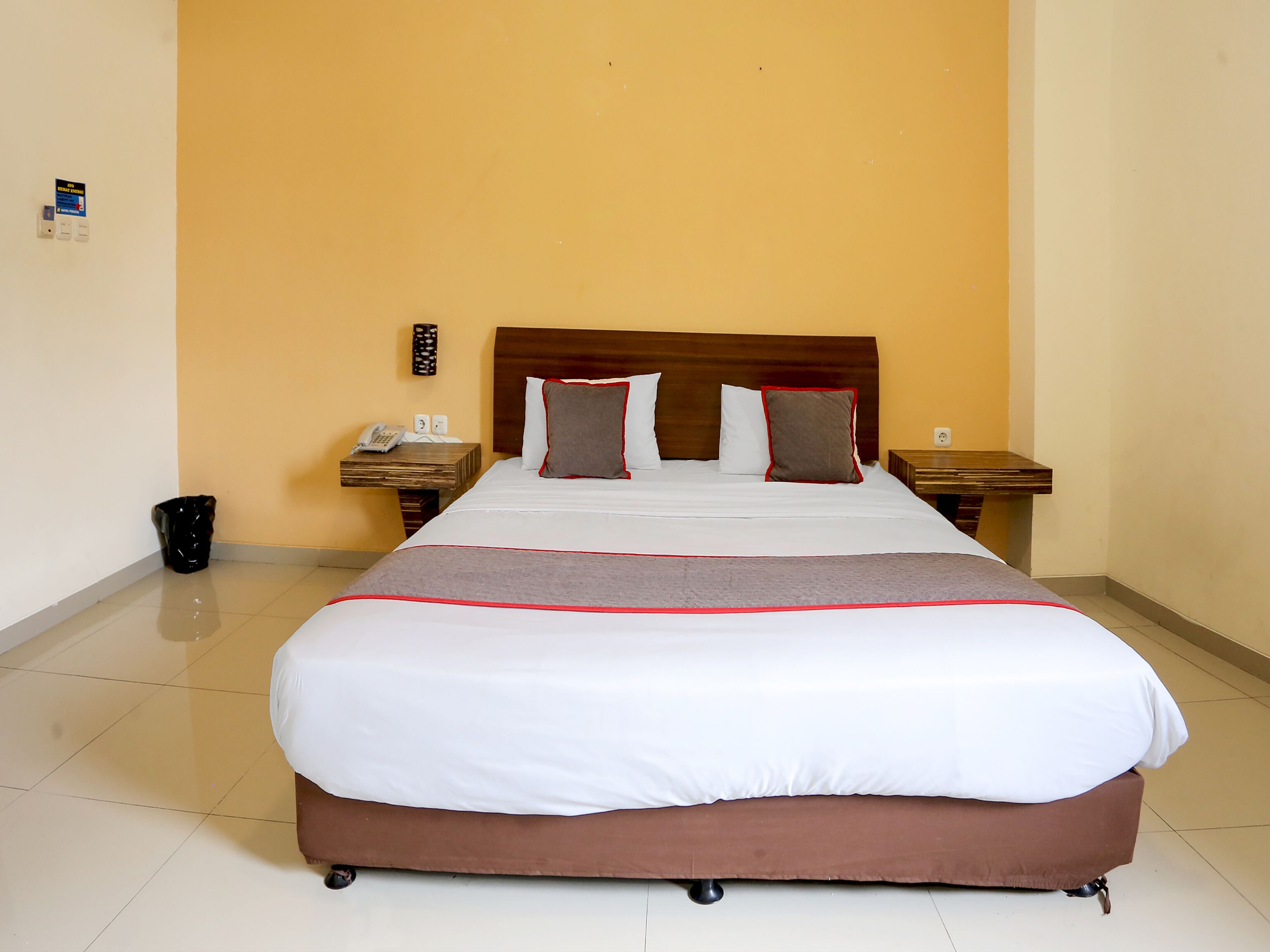 Ein Hotelzimmer mit einem großen Bett, zwei Nachttischen, einem Telefon und einem Mülleimer.