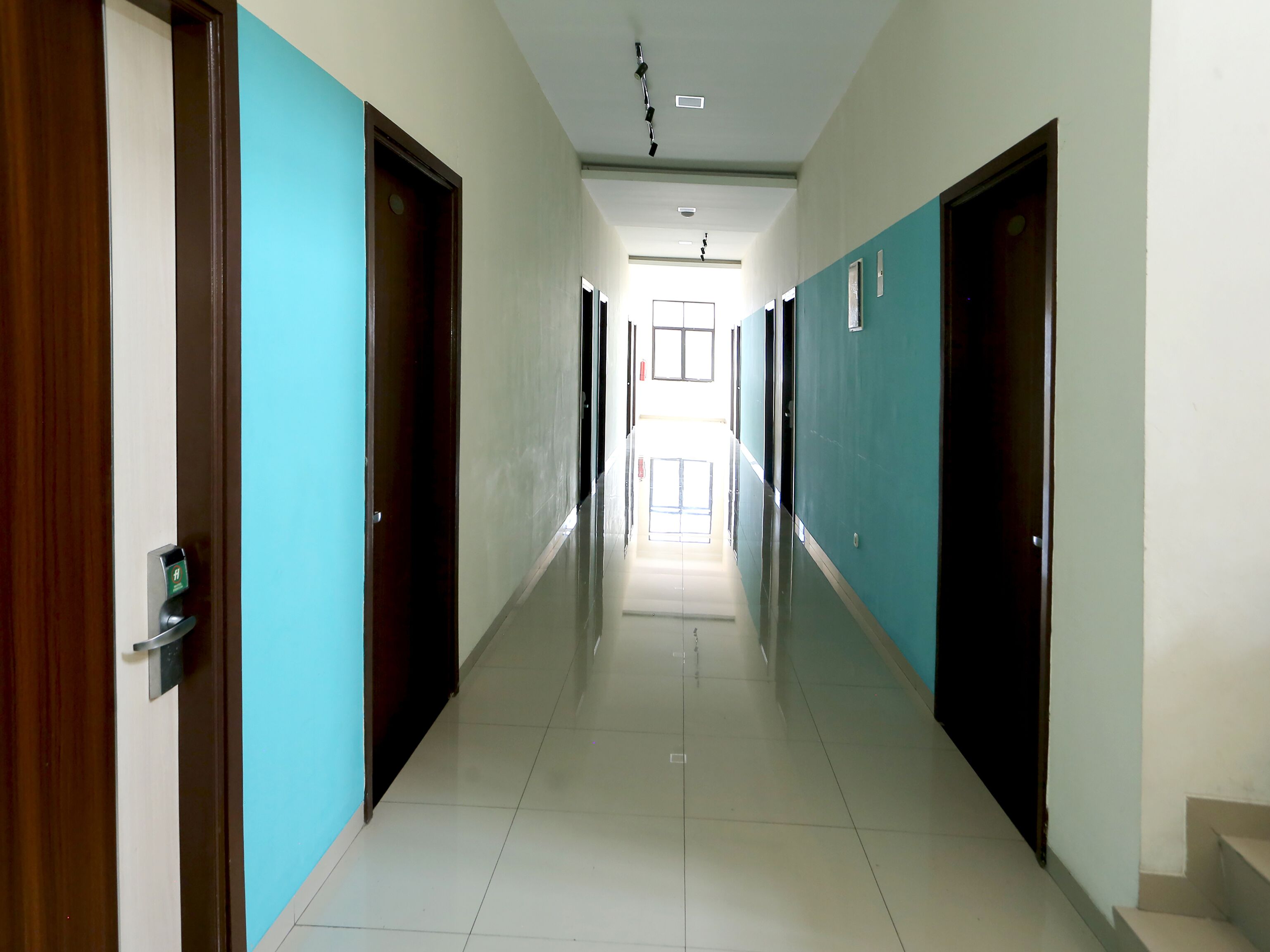 A long, narrow hallway with doors on both sides, leading to a bright room at the end.