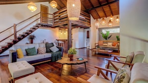 A spacious living area with a wooden staircase, a sofa set, a coffee table, and hanging pendant lights. - Casa OluOlu Itacaré (Itacaré)