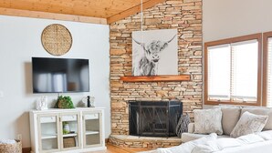 Un salon avec une cheminée en pierre, un canapé blanc et un plafond en bois.