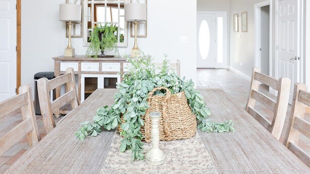 Un coin repas avec une table en bois, des chaises, un panier décoratif contenant des plantes et un miroir au-dessus de la table.