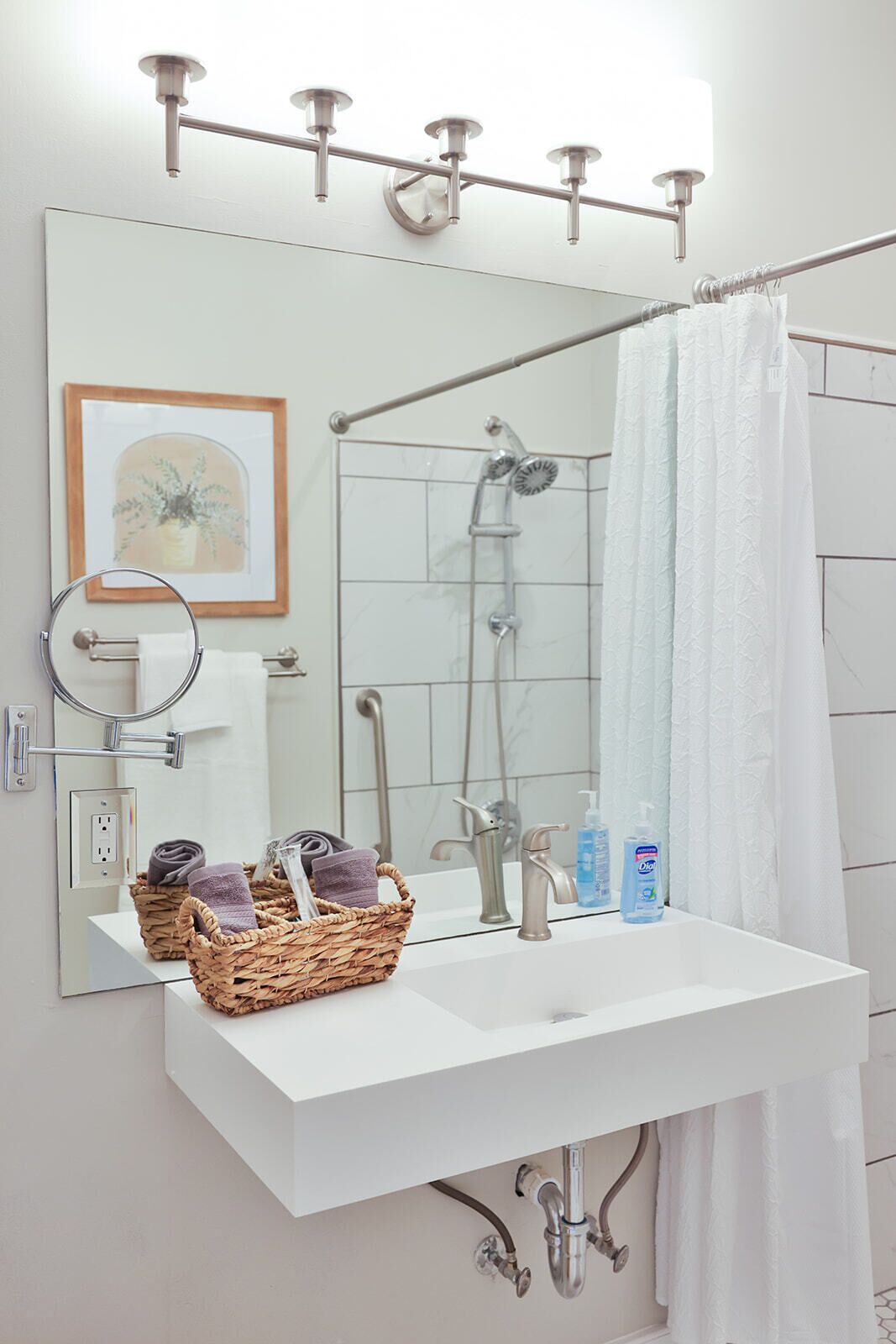A bathroom with a white sink, a mirror, a shower, and a towel rack.