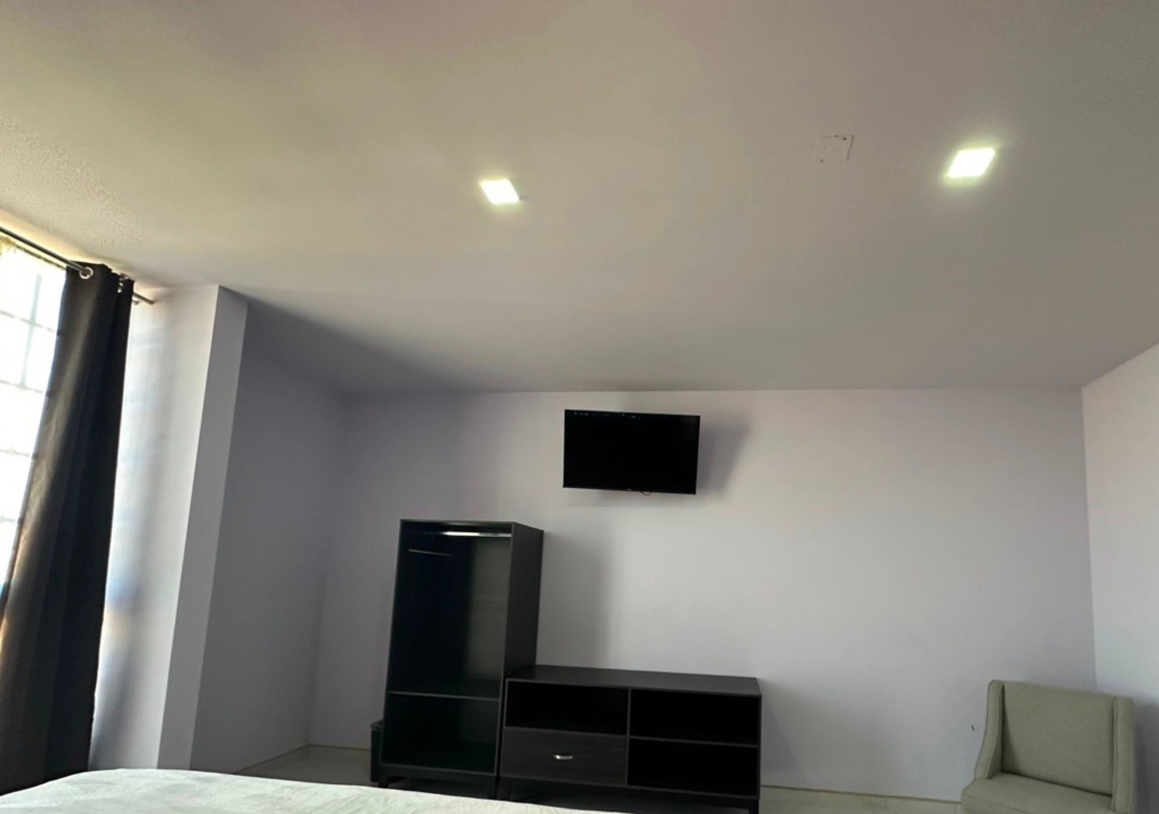 Una habitación con cama, televisión montada en la pared, armario y una silla.