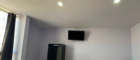 Una habitación con cama, televisión montada en la pared, armario y una silla.