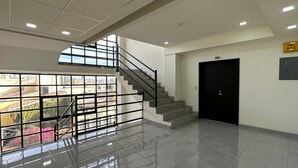 A modern interior with a staircase leading to an upper level, a black door, and a view through large windows. - Hotel Maricela (San Juan de los Lagos)