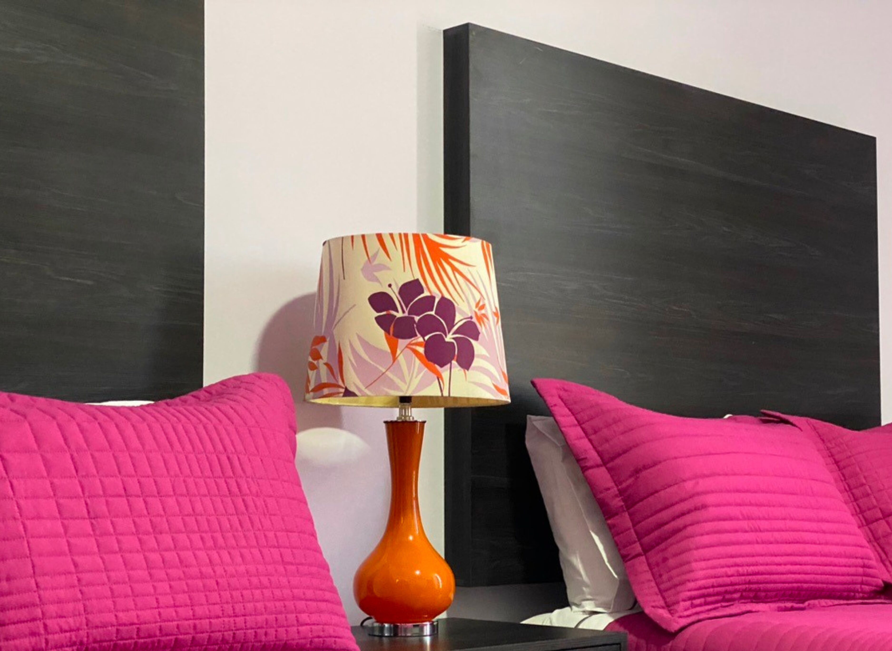 Une chambre moderne avec une tête de lit noire, un vase décoratif orange et une literie rose.