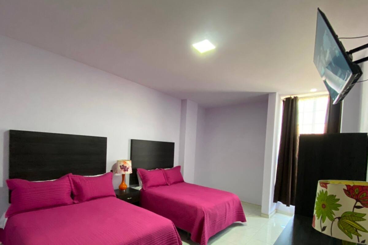A hotel room with two beds, a TV, and a lamp.
