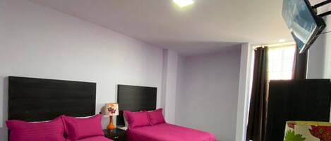 A hotel room with two beds, a TV, and a lamp.