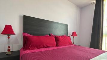 A bed with a dark headboard, two red lamps, and a window with curtains.
