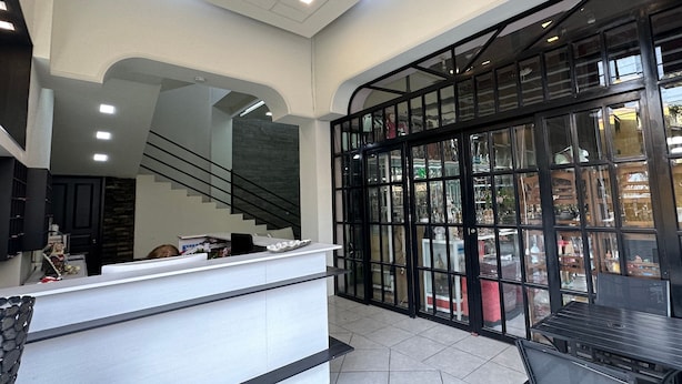 A hotel lobby with a reception desk, a staircase, and a glass partition with a view of the street. - Hotel Maricela (San Juan de los Lagos)