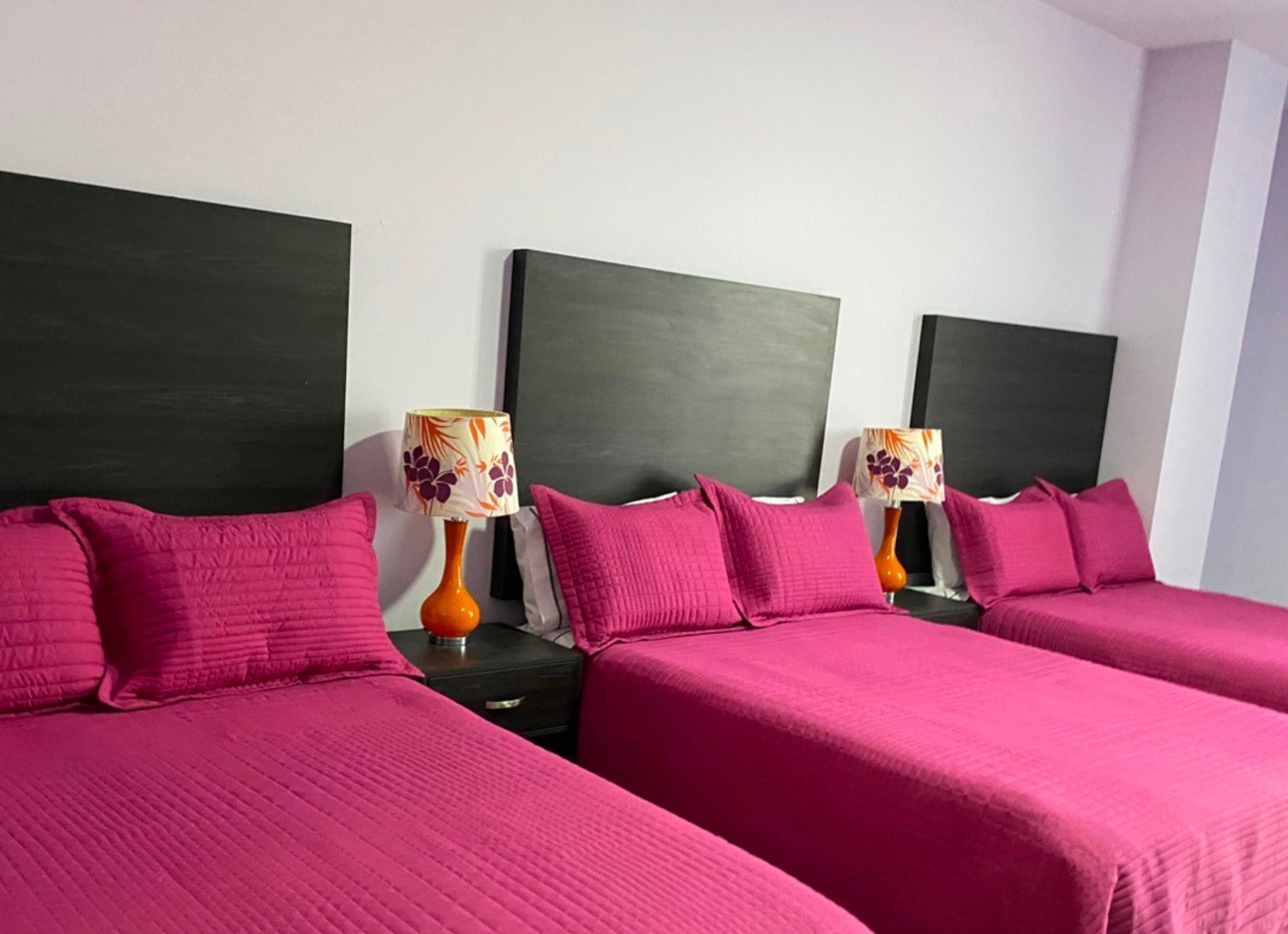 Ein Hotelzimmer mit zwei Betten, jeweils mit dunklem Kopfteil und rosa Bettwäsche. Auf den Nachttischen stehen zwei Lampen mit floralen Lampenschirmen.