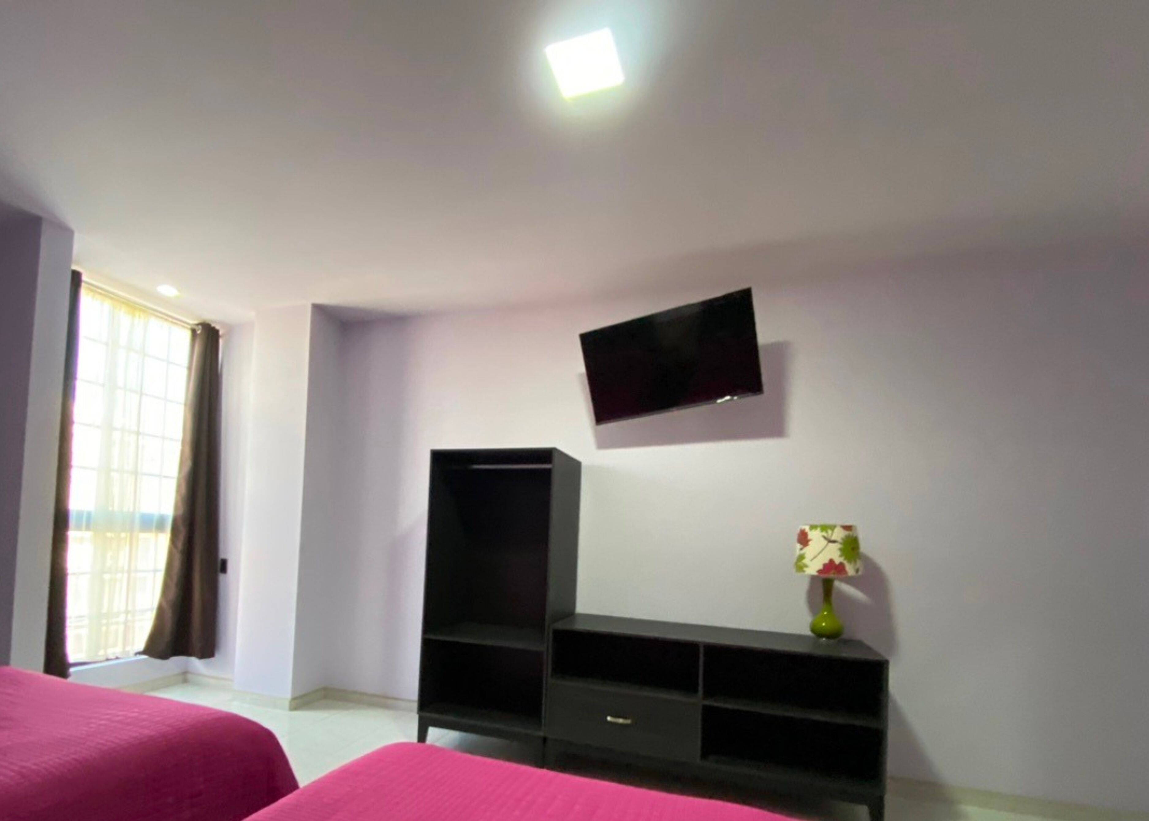 Een slaapkamer met twee bedden, een aan de muur bevestigde televisie, en een tafeltje met een vaas.