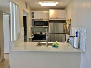 A compact kitchen with white cabinets, a stainless steel refrigerator, a microwave, and a sink.