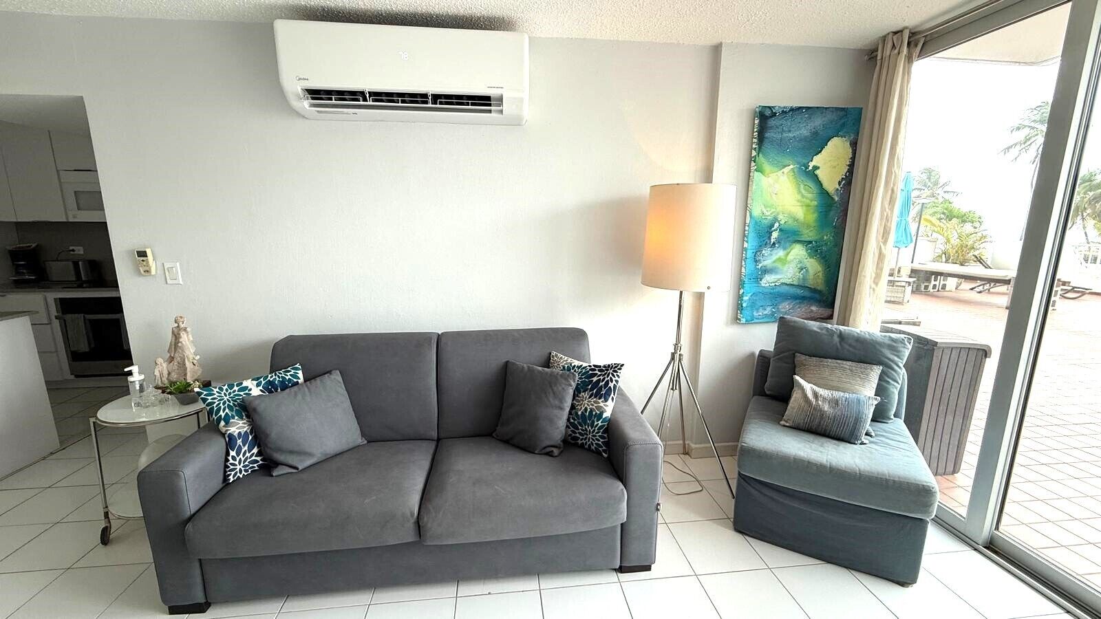 Un salón con un sofá gris, un sillón gris más pequeño, una lámpara de pie y un cuadro en la pared.
