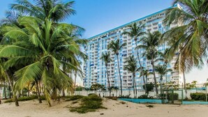 A beachfront hotel with multiple floors, palm trees, and a sandy beach. - MB2E-Unique Terrace Two Bedrooms-Pool & Ocean View (Carolina)