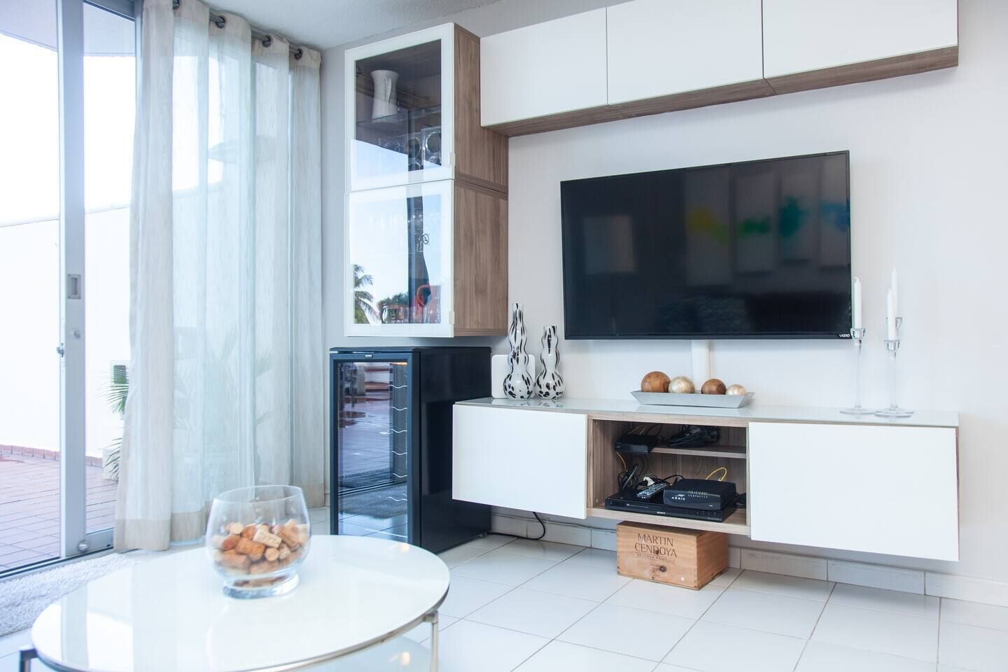 Eine moderne Küche mit integriertem Fernseher, einem Glastisch und einer Obstschale sowie einer Glastür zum Balkon.