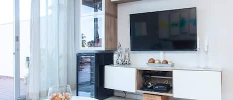 Eine moderne Küche mit integriertem Fernseher, einem Glastisch und einer Obstschale sowie einer Glastür zum Balkon.